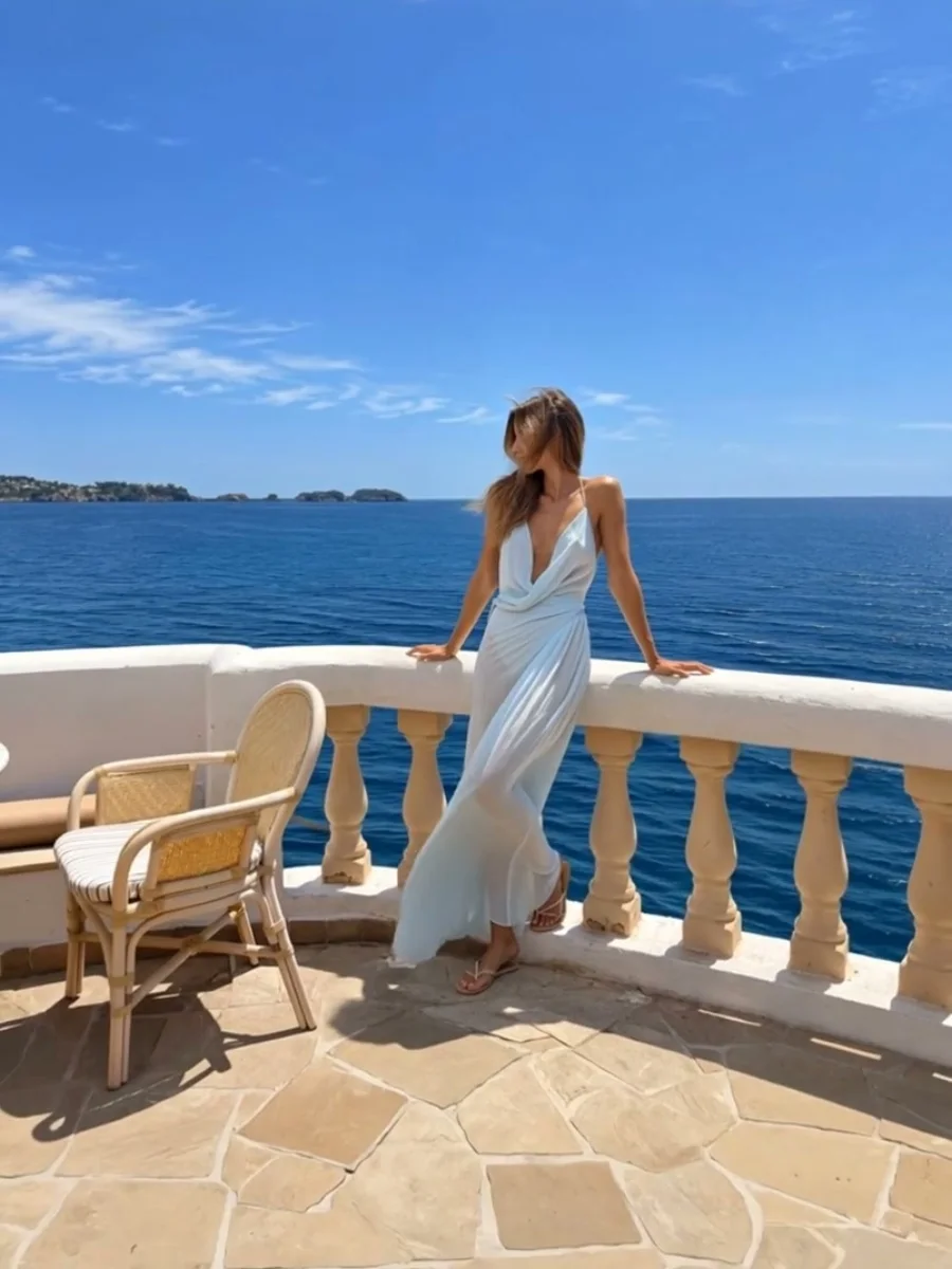 The photo: she leans on a white balustrade over a deep blue sea, dress caught in the breeze